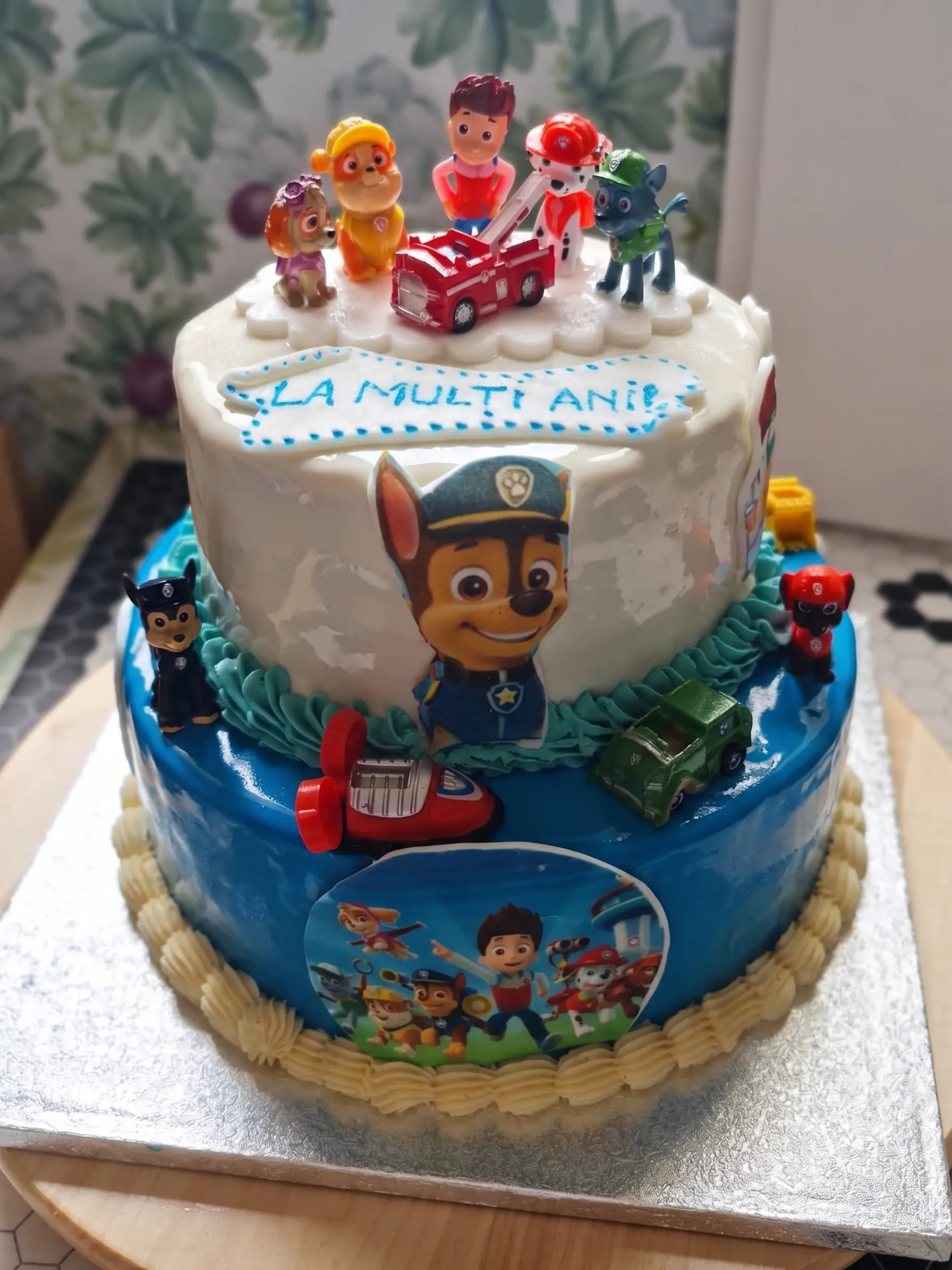 Two-tier children’s birthday cake decorated with rescue pup figures, vehicle details and blue icing accents